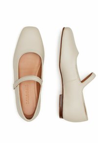 Zapatos Mary Jane color crema hechos de cuero con puntera cuadrada, cortes curvados y una tira en el empeine, que cuentan con un tacón de madera bajo.