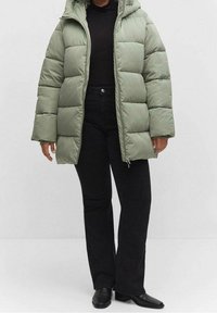 Hellgrüne Steppjacke mit Kapuze, mit einem gesteppte Design. Kombiniert mit schwarzen Schlaghosen und schwarzen spitzen Stiefeln.