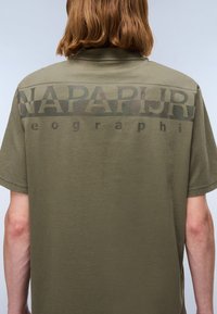 Oliven grønn bomulls t-skjorte med et stort kamuflasjemønstret "NAPAPIJRI"-logo på baksiden, med korte ermer og en avslappet passform.