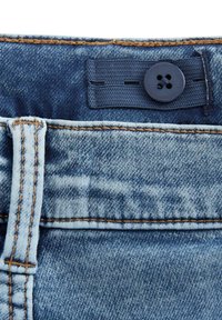 Sinivärvi denim vöökohaga, millel on reguleeritav elastne rihm ja tumehall nupp, millel on oranž õmblus ja vöölõng.