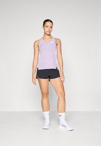 Lichtpaarse sporttop met een gestructureerd patroon, gecombineerd met zwarte shorts. Witte sportschoenen en sokken maken de outfit compleet.