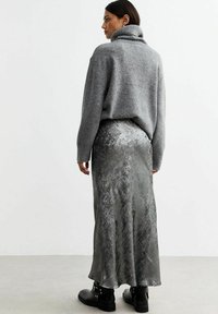 Un pull à col roulé en tricot gris associé à une jupe métallisée argentée et élégante. Des bottines noires brillantes à la cheville complètent le look.