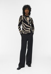 Zwarte en beige trui met zebra-stripes, gebreide textuur, ronde halslijn, gecombineerd met zwarte wijde broek en glanzende zwarte schoenen.