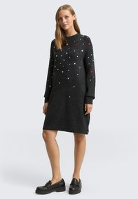 Dunkelgraues gestricktes Kleid mit langen Ärmeln, das über verstreute weiße und rote Herzmuster verfügt und eine lockere Passform hat, die bis zur Mitte des Oberschenkels reicht.