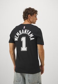 Sort NBA-trøje med "WEMBANYAMA" og nummer "1" i hvid tekst. Lavet af stof med en sporty pasform og korte ærmer.