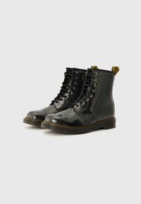 Botines de tobillo negros con purpurina, acabado liso, puntera redonda, diseño de cordones y lengüetas amarillas. Cuenta con una gruesa suela de goma negra.