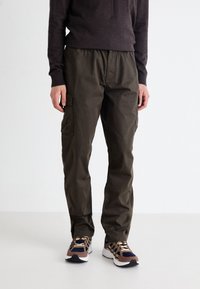Olijfgroene cargobroek met een ontspannen pasvorm, voorzien van zijzakken, een drawstring tailleband en duurzaam katoen. Een paar gemusterde sneakers zichtbaar.