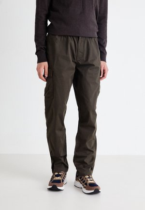 Olive green cargo pants with a relaxed fit, featuring side pockets, a drawstring waistband, and durable cotton fabric. Pair of patterned sneakers visible.