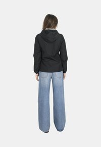 Giacca nera con cappuccio dal taglio aderente, abbinata a jeans in denim blu a gamba larga con tasche posteriori.