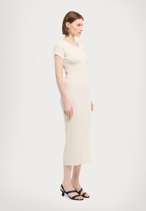 Ribbed, kermaanuinen mekko, jossa on lyhyet hihat ja istuva siluetti, joka ulottuu polven keskiväliin. Mekko on yhdistetty mustiin, nauhalla varustettuihin korkokenkiin.