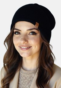 Gorro de punto negro con puño doblado y acabado texturizado; presenta un pequeño detalle de etiqueta de cuero marrón.