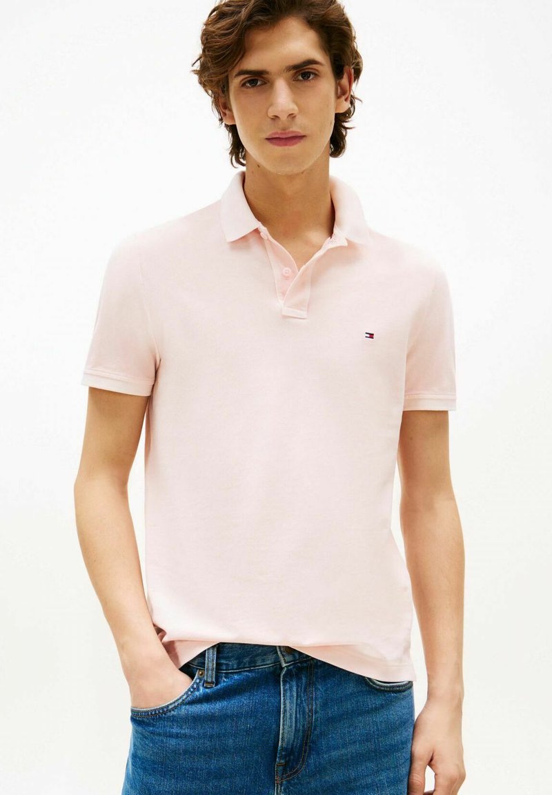 Polo rosa chiaro in cotone con colletto e maniche corte, con un piccolo logo sul petto e abbinata a jeans blu.