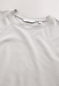 Vaaleanharmaa pyöreäkauluksinen t-paita, joka on valmistettu pehmeästä puuvillasta ja jossa on sileä pinta sekä minimalistinen muotoilu. Labelissa näkyy merkki "NEXT" ja koko "M".