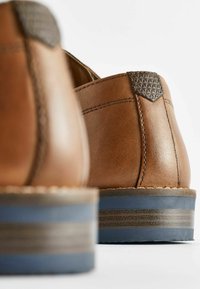 Zapatos de cuero marrón con un acento texturizado gris en el talón, con una suela a rayas en azul claro y marrón. Acabado suave y costuras detalladas.