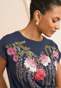 T-shirt blu navy a maniche corte con ricami floreali colorati in rosa, bianco e verde. Tessuto in cotone morbido con una vestibilità morbida.