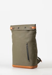 Zaino verde oliva realizzato in materiale resistente con design a risvolto, tasca con zip nera e dettagli in pelle marrone chiaro alla base e alle cinghie.