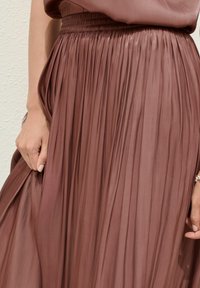 Plisovaná midi sukňa v jemnej fialovej farbe, vyrobená z ľahkého materiálu. Obsahuje elastický pás a splývavý strih s jemným leskom.