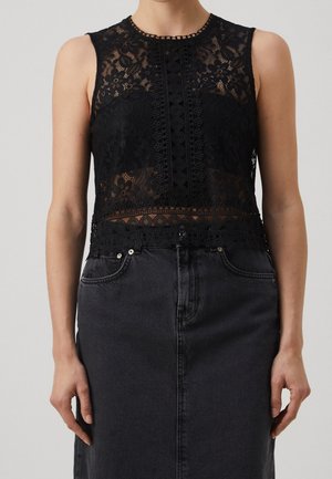 Woman wearing a sleeveless black lace top with floral patterns paired with a high-waisted dark denim skirt.
