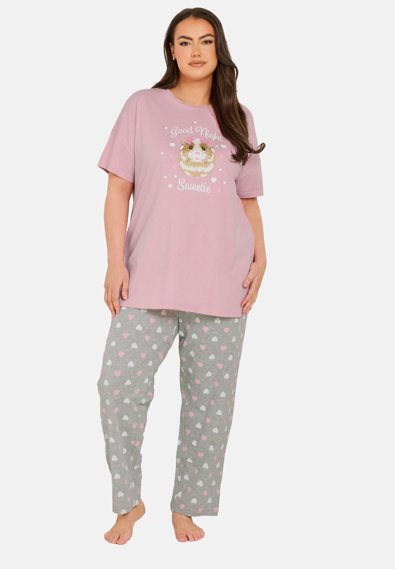 Rosaröd pyjamasöverkort med grafisk design; gråa byxor med hjärtformade mönster i rosa och vitt. Materialet verkar mjukt och bekvämt.