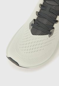 Αθλητικό παπούτσι ανοιχτού γκρι με αναπνεύσιμο πλέγμα στο πάνω μέρος, διαθέτοντας κορδόν�ια και λεπτομέρειες σε σκούρο γκρι και υφή στη σόλα για καλύτερη πρόσφυση.