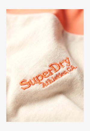 Light beige fabric with an embossed orange “SuperDry Athletics, CA” logo. Smooth texture with subtle shading and creases.