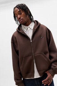 Felpa con zip marrone realizzata con tessuto morbido, con cappuccio regolabile con coulisse, due tasche frontali e una piccola etichetta con logo sul petto.