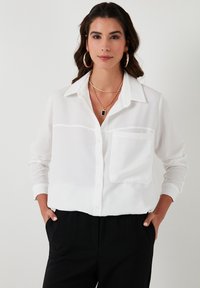 White button-up shirt with a collar, single chest pocket, and long sleeves. Fabric appears lightweight and slightly sheer.