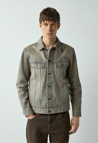 Džinsa jaka izbalējusi olīvzaļā krāsā ar klasisku apkakli, pogām priekšpusē, divām krūšu kabatām un sānu šķēlumiem. Gluda tekstūra ar minimālu noformējumu.