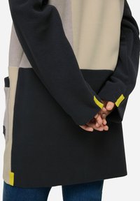 Kurtka polarowa w blokowych kolorach w ciemnoszarym, jasnoszarym i beżowym; posiada żółty akcent na mankiecie oraz boczną kieszeń.