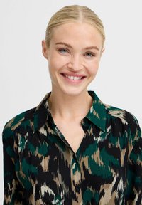 Camicia multicolore con un motivo astratto nero, verde e beige. Presenta un colletto classico e una chiusura con bottoni, realizzata in tessuto leggero.