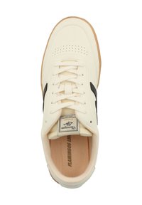 Cream-colored sneaker with black accents, perforated toe, and white laces. Features a tan rubber sole and a label on the tongue.