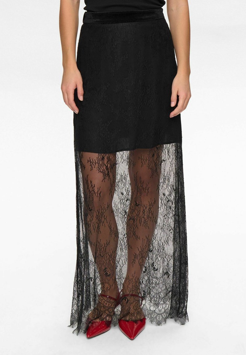 Melna mežģīņu svārki ar caurspīdīgu pārklājumu, kuram ir ceļa garuma iekšējā kārta un ziedu raksti. Saskaņoti ar sarkanām augstpapēžu kurpēm.