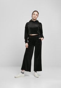 Svart velour loungewear-sett som inkluderer en cropped hettegenser og brede bukser, begge med en myk tekstur. Kombinert med hvite sneakers og stripete sokker.