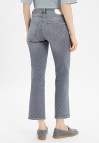 Grijs denim jeans met een subtiele patroon, verkorte broekspijpen, standaard zakken en een logo label op de tailleband. Schoenen zijn grijze instap schoenen.