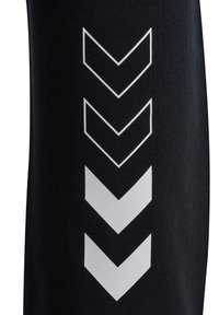 Czarne spodnie sportowe z białym wzorem w kształcie szewrona wzdłuż boku. Wykonane z elastycznego materiału o gładkiej fakturze.