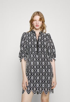 Melnā kleita ar baltajiem ziedu dimantu rakstiem, īsām pūkainām piedurknēm un viļņotu apakšmalu. Iekļauj V veida izgriezumu un dekoratīvu saiti.