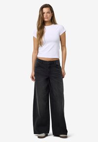 Zwarte wijduitlopende jeans van denim, met een hoge taille, voorzakken en een vervaagde afwerking. Gecombineerd met een getailleerd wit T-shirt.