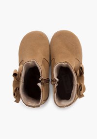 Botas de tobillo de ante color beige con un interior suave, un lazo decorativo y cremallera lateral. Textura lisa con un diseño de punta redondeada.