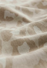 Bomullstyg i beige med ett ljusbrunt leopardmönster; mjuk textur med synliga ribbor och veck.