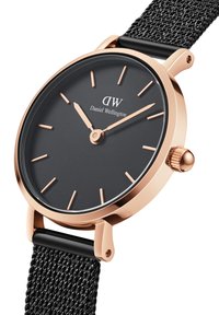 Black watch with a round, matte dial, gold-tone hands and indices. Features a woven black mesh strap and a gold-tone case with a crown.