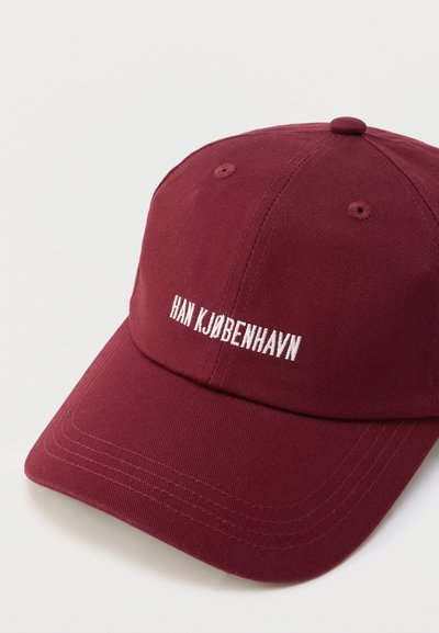 Bordó pamut sapka ívelt napellenzővel, elöl fehér hímzett "HAN KJØBENHA VN" felirattal. Varrt díszítésekkel.