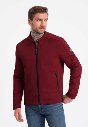 Bordeaux zip-up jakke med høj krave, tekstureret stof, sorte detaljer og sidelommer med lynlås, båret sammen med en struktureret sweater underneath.