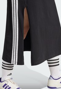 Črna atletska krila z bočnim razporkom in tremi belimi črtami. V kombinaciji z belimi nogavicami in supergami z vijoličnimi detajli.