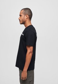 Črna bombažna majica s kratkimi rokavi, na sprednji strani z bold belimi črkami "VARNOST". Kroj je klasičen in sproščen.