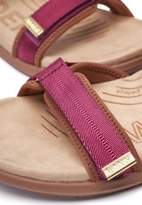 Ruske flip-flop sandale s teksturiranim, svijetlosmeškim uloškom i ružičastim tekstilnim trakama, koje imaju zlatni akcent, naglašavajući ugravirani logo.