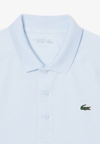 Ljusblå pikétröja i bomullsblandning, med klassisk krage, tre knappslå och grön broderad krokodil-logotyp på bröstet.