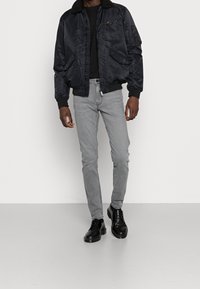 Svart bomberjacka med mjukt krage, ficka med dragkedja, matchad med smala grå jeans och svarta skor. Slät textur, avslappnad design.