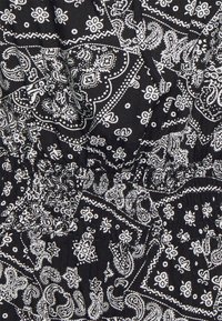 Svart tyg med ett vitt bandana-mönster som har paisley- och blommönster, samlat vid midjan med elastik för en figurnära design.