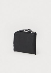 Pochette nera compatta con zip, dotata di un tirazip intrecciato bianco e nero, su uno sfondo chiaro e semplice.