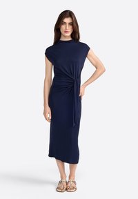 Vestido azul marino, hasta la rodilla, con silueta ajustada, mangas cortas y detalle de nudo en la cintura. Tejido suave y elástico, textura lisa.